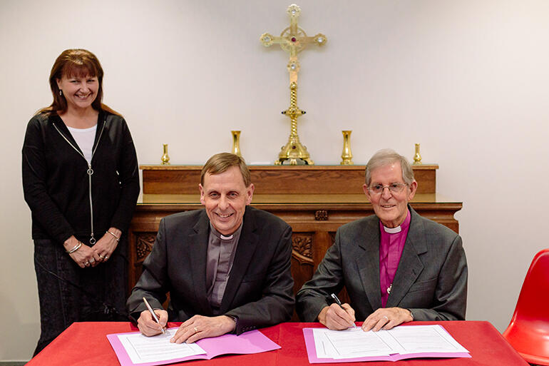 The bishop-elect signs up before two witnesses - his dad, Bishop Brian Carrell, and his wife, Teresa Kundycki-Carrell.