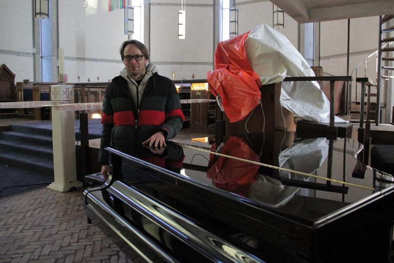 St Paul's Cathedral Director of Music Michael Grant stands at the piano that survived under salvage sheets, the organ is yet to be fully assessed.