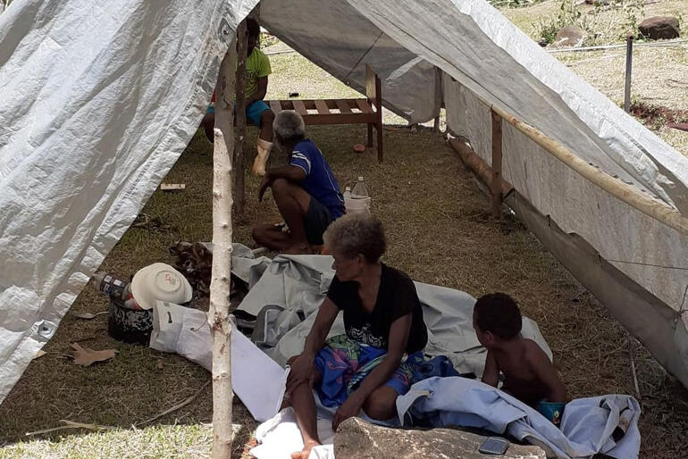 A group of people in Dreketi shelter under sheeting after cyclone damage to their home. 
