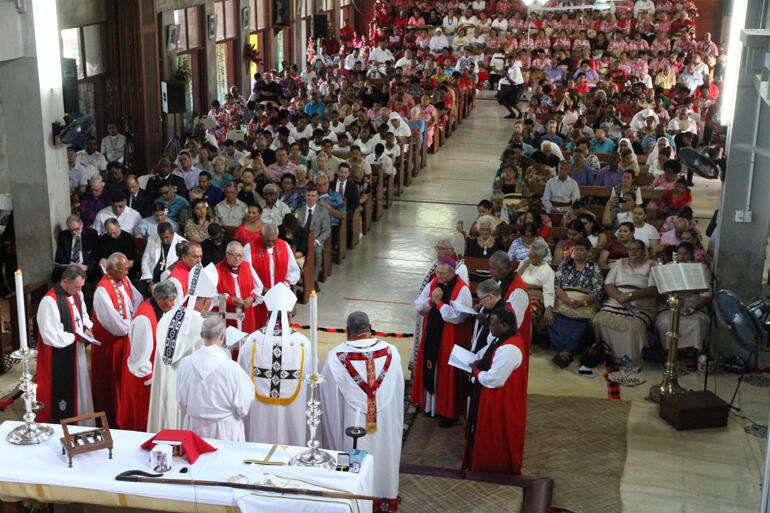 Bishops gather in the sanctuary, obscuring Fr Sione who kneels before the altar.